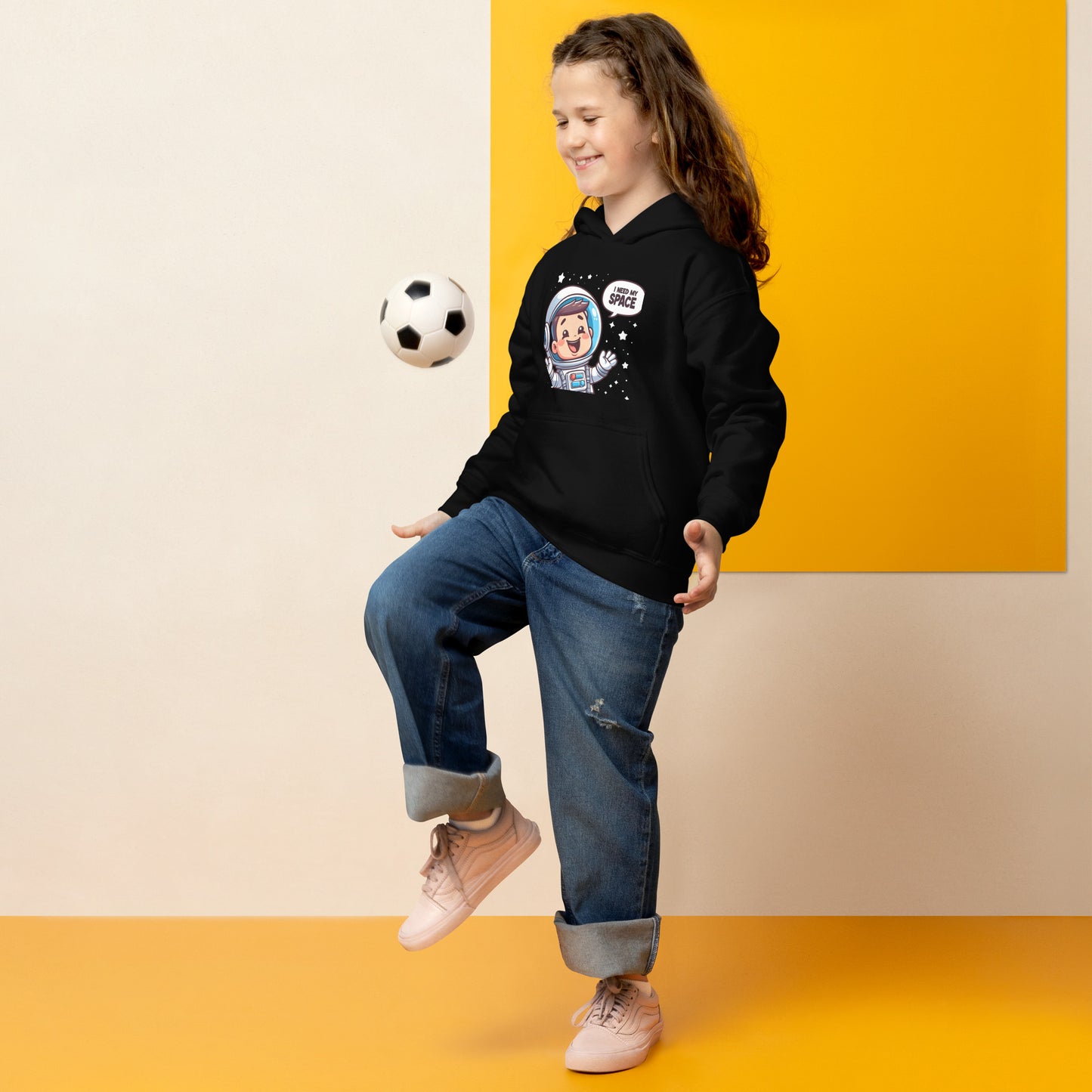 Child wearing a heavy blend space hoodie in black while playing with a soccer ball indoors