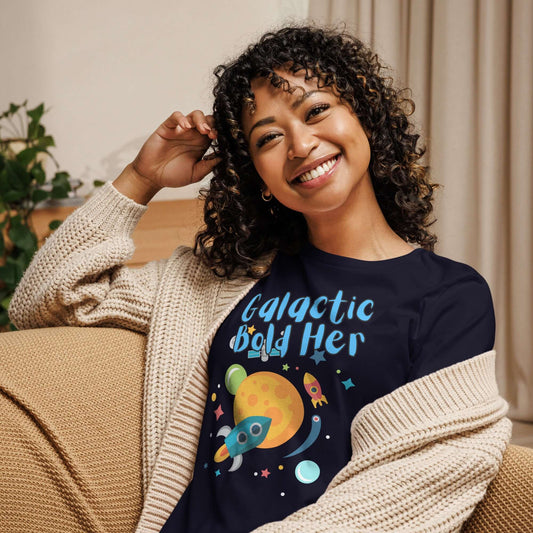 Woman wearing a navy blue t-shirt with 'Galactic Bold Her' design, smiling and cozy in a cardigan.